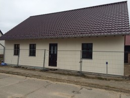 Ein kleines Haus mit braunem Dach und einem Zaun im Bau.