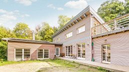Ein Elite-Holzbau-Haus, eingebettet in ein Waldgebiet, komplett mit Terrasse.
