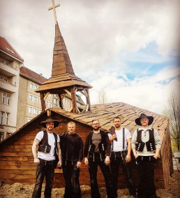 Eine Gruppe Männer steht vor einer Holzkirche.